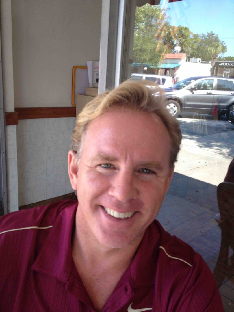 A man with blonde hair and wearing maroon shirt.