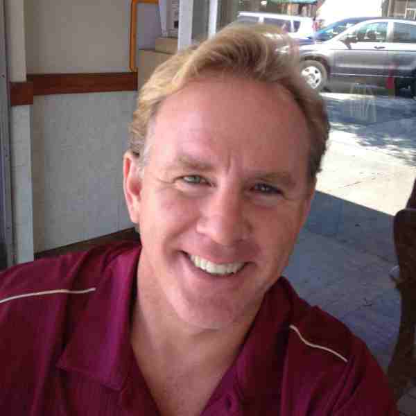 A man with blonde hair and wearing a maroon shirt.